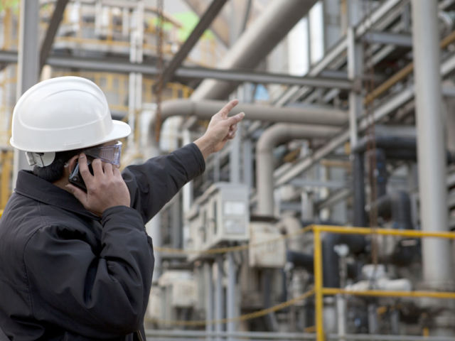 man in hardhat pointing up at pipelines